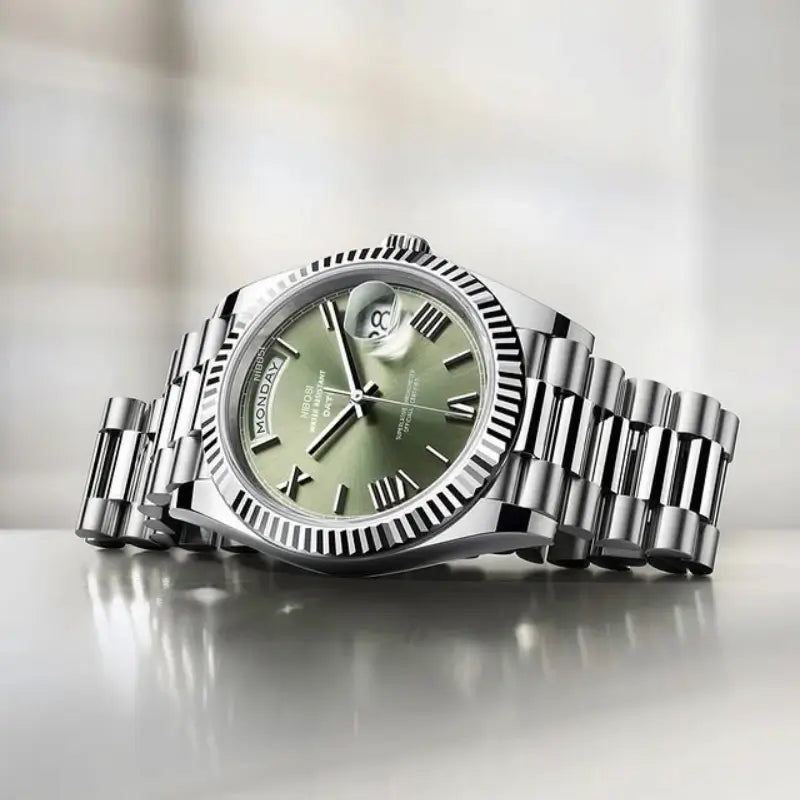 VEXO Day Date Olive watch with sunburst green dial, Roman hour markers, magnified calendar, and polished steel bracelet on reflective surface